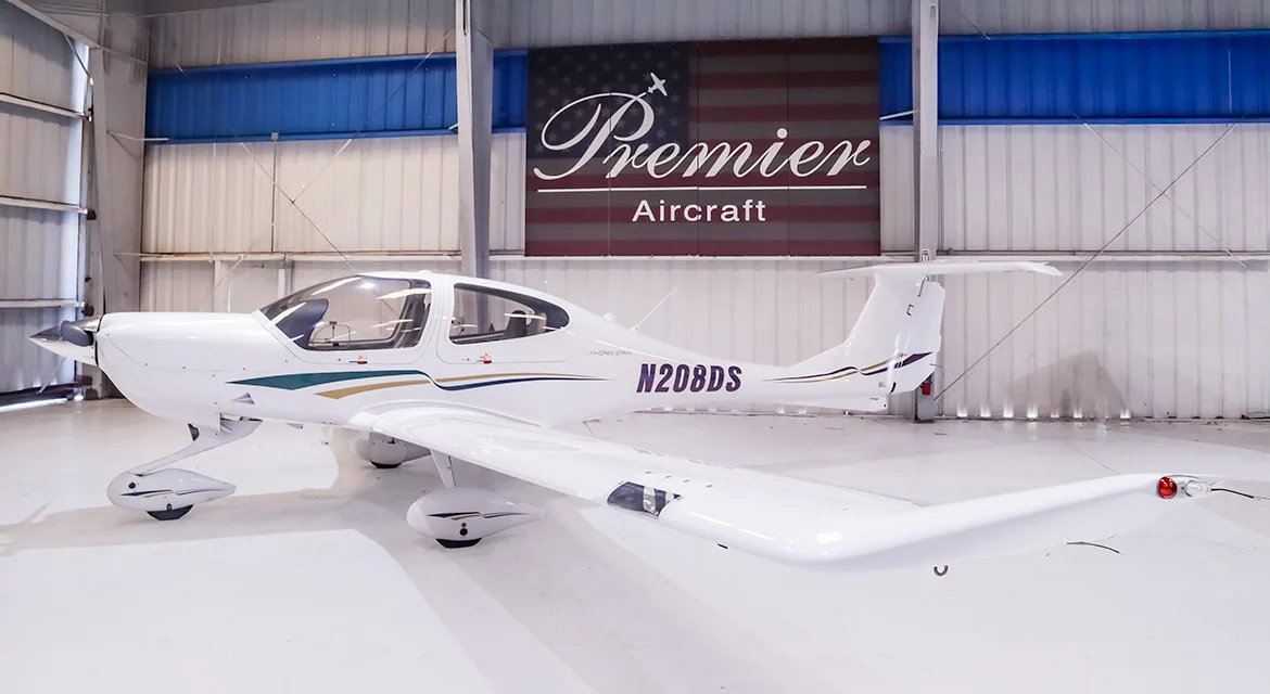 A white Diamond DA40 Star aircraft with green, gold, and purple stripes, registration N208DS, parked in a hangar.