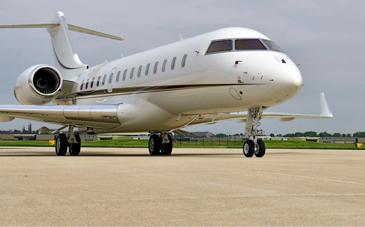 A white business jet with a gold stripe is parked on a tarmac, viewed from the front-right.