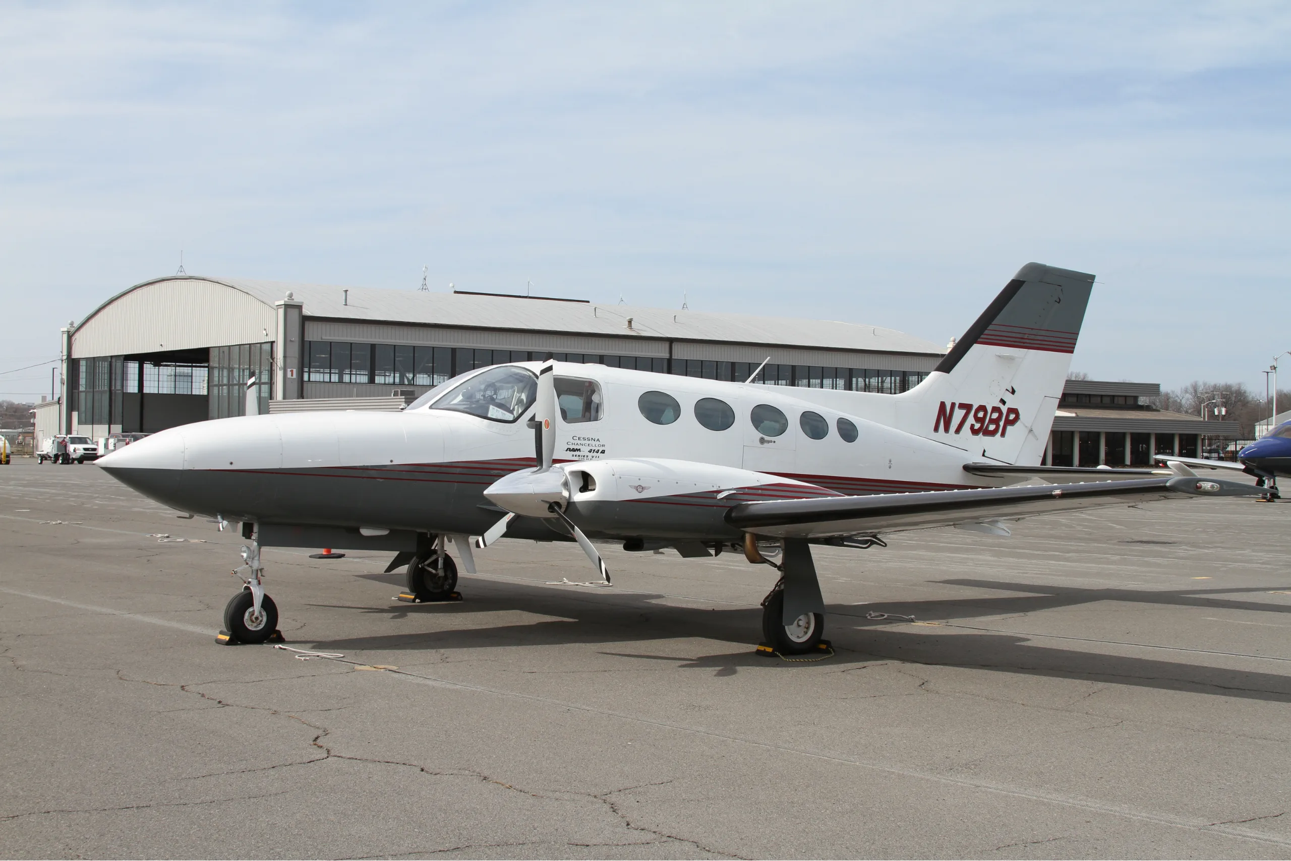 A white and gray Cessna aircraft is parked on the tarmac in front of a hangar.