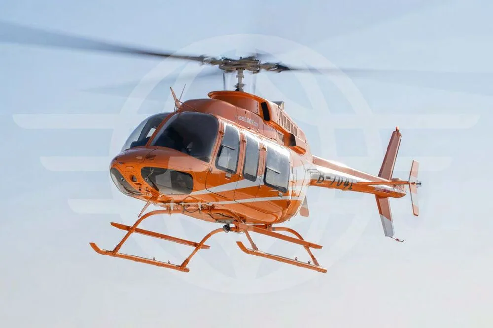 An orange Bell 407EXP helicopter with registration B-704L flies against a clear blue sky, viewed from the front-right.
