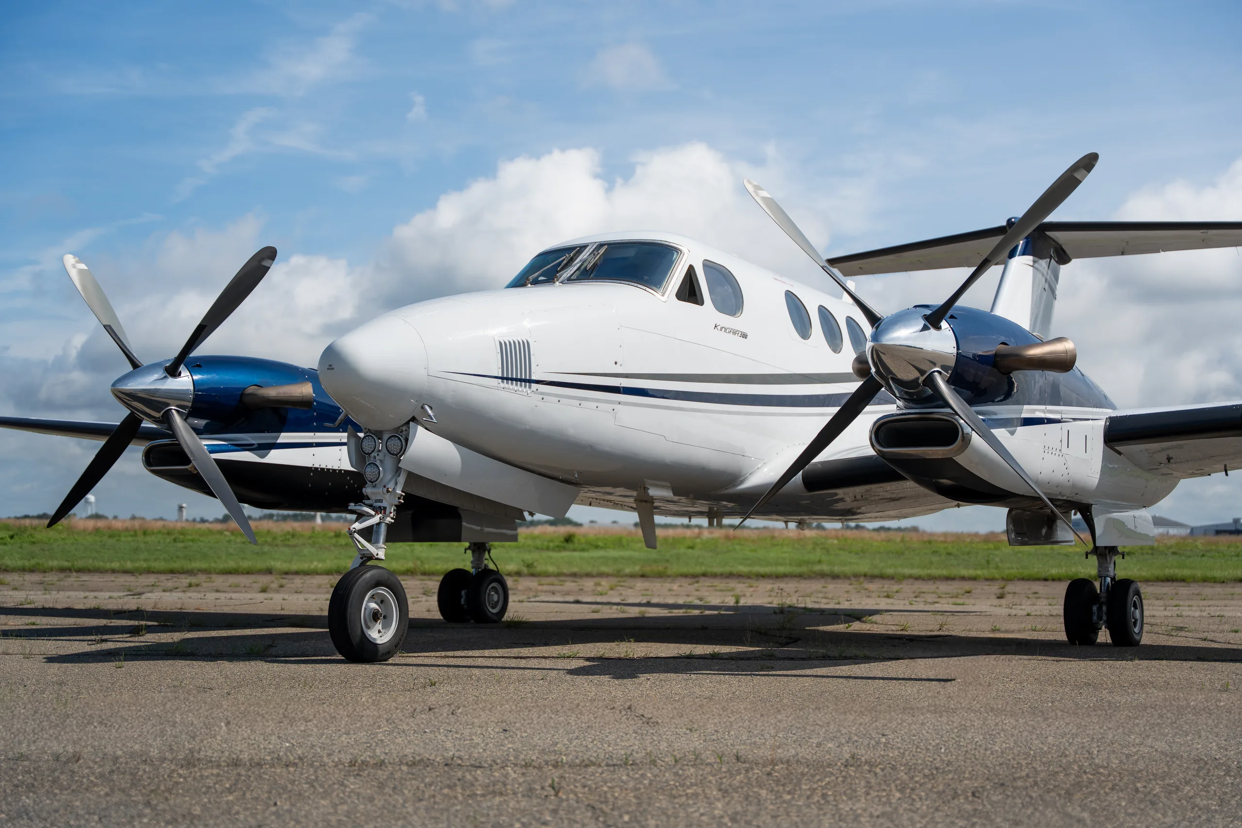 A close-up front-side view of a white and blue Beechcraft King Air twin-turboprop aircraft on a tarmac.