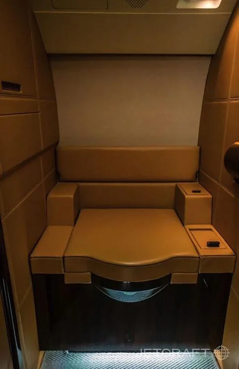 A tan leather seat in a small compartment, possibly a lavatory or crew rest area, within a business jet.