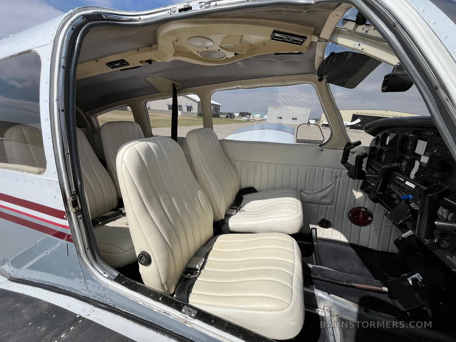 The interior cabin of a light aircraft, showing four cream-colored leather seats and the open door.