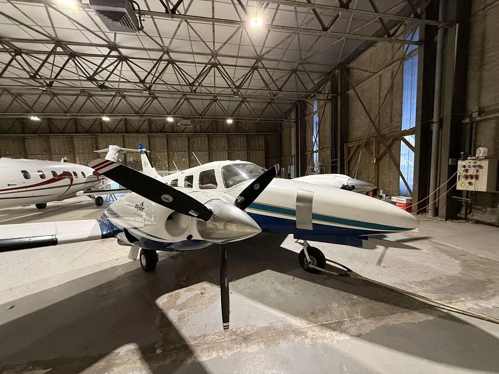 Front-right view of a white and blue Piper Seneca twin-engine propeller aircraft parked in a hangar.
