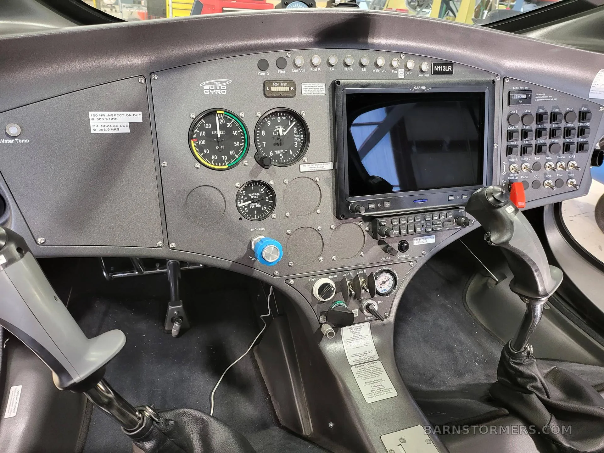 A detailed view of the gyrocopter cockpit, featuring a Garmin display, analog gauges, and flight controls with registration N113LR.
