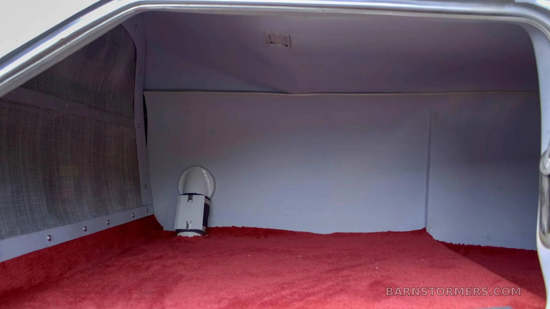 An empty aircraft baggage compartment with a red carpeted floor and light gray walls.