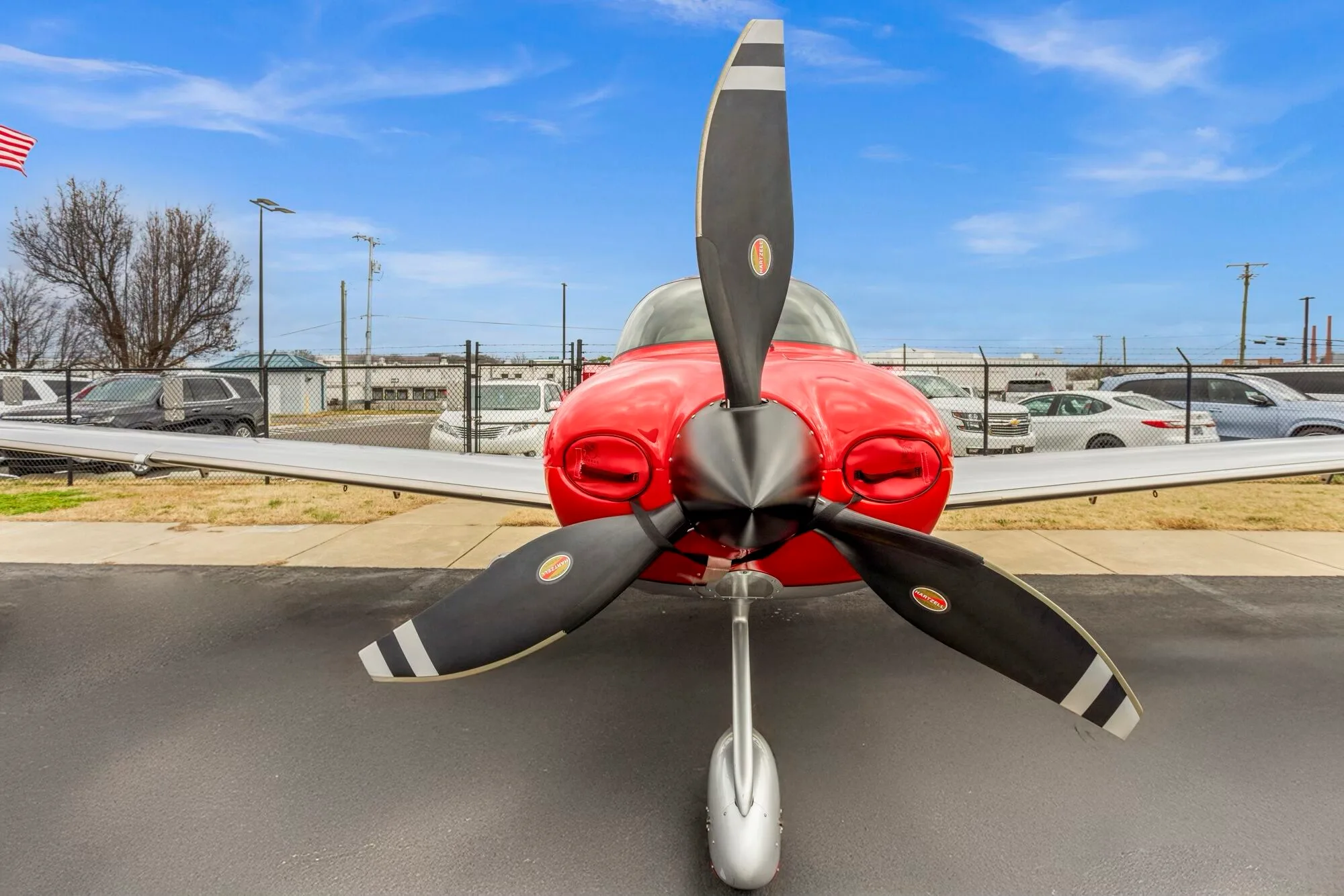 A close-up front view of the propeller and nose of a red and silver Cirrus SR22 aircraft.