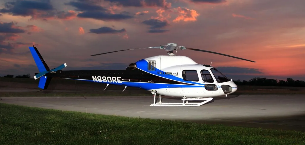 A white and blue helicopter with registration N880RE sits on a tarmac at sunset.