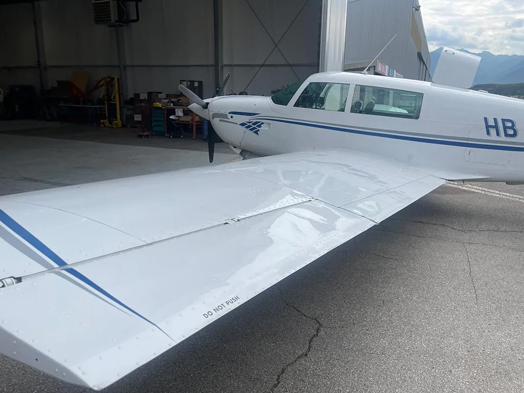 Top view of the wing and fuselage of a white aircraft with blue stripes, parked inside a hangar.