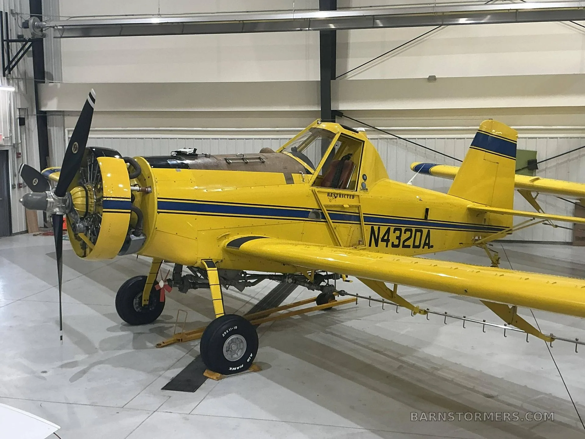 A yellow agricultural aircraft with blue stripes, registration N432DA, parked inside a hangar.