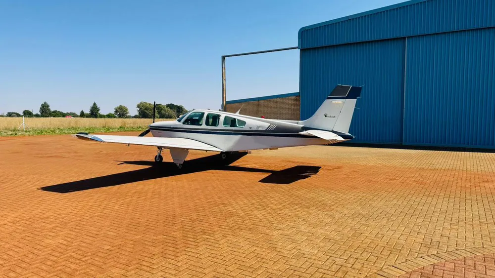 A white and dark grey single-engine propeller aircraft parked in front of a large blue hangar.