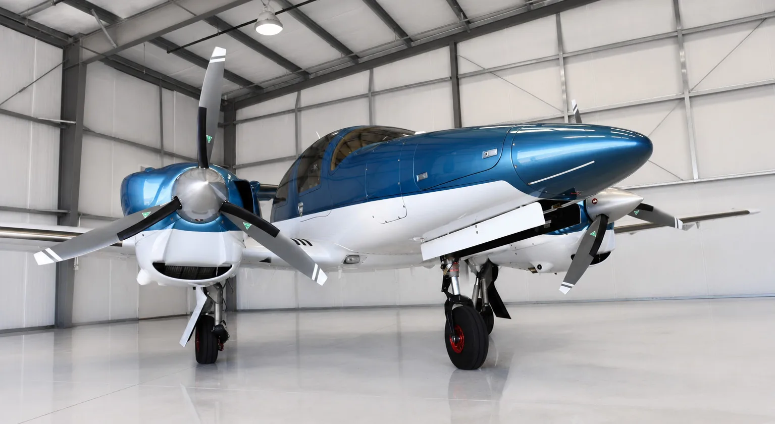 A front view of a blue and white Diamond DA62 aircraft with twin propellers in a hangar.