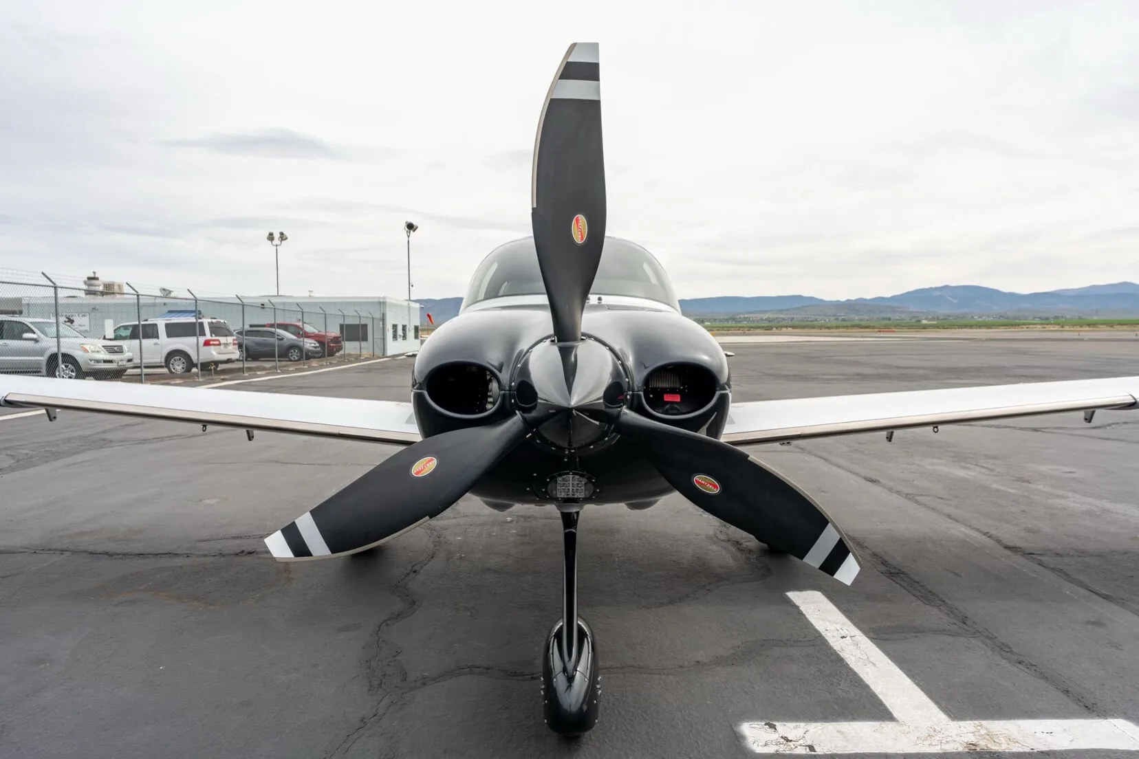 Front view of a black, blue, and silver single-engine aircraft with a three-bladed propeller on an airfield.