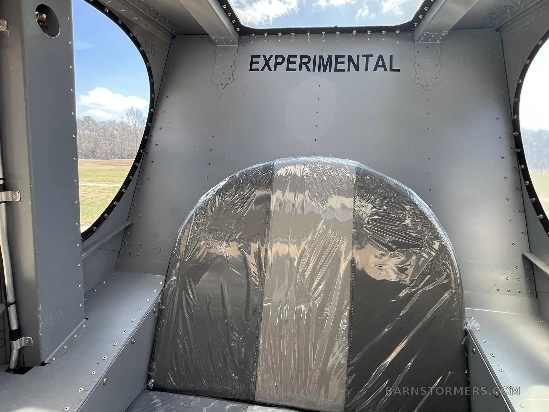 The interior of an experimental aircraft cabin with a plastic-covered seat and "EXPERIMENTAL" stenciled on the ceiling.