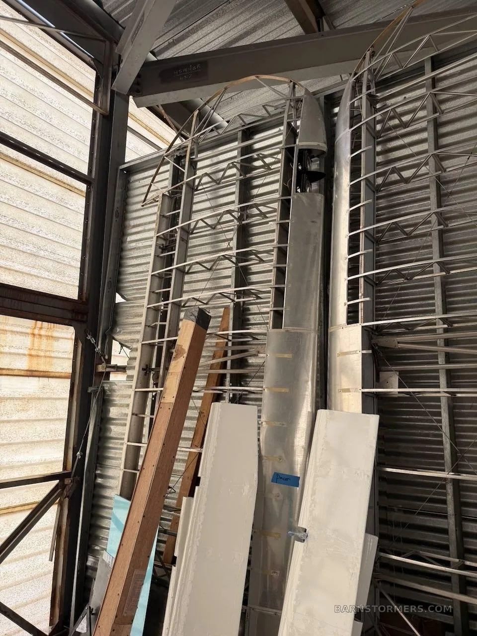 Aircraft wing and fuselage frame components stored vertically in a metal hangar.