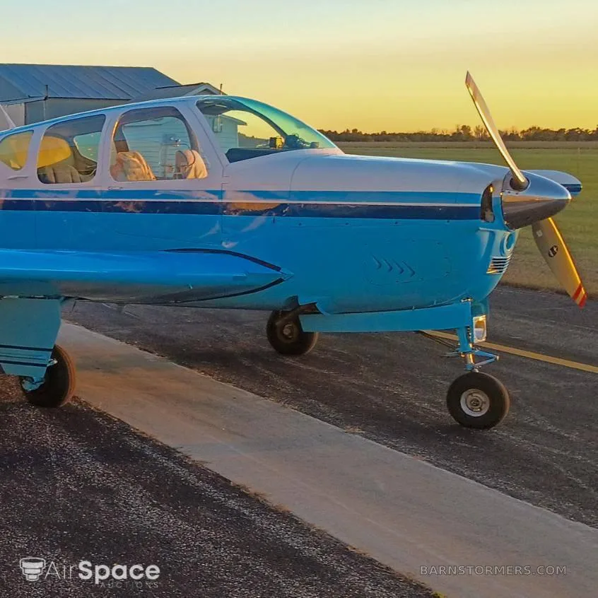 A light blue and white single-engine aircraft with a propeller, parked on a tarmac at sunset.