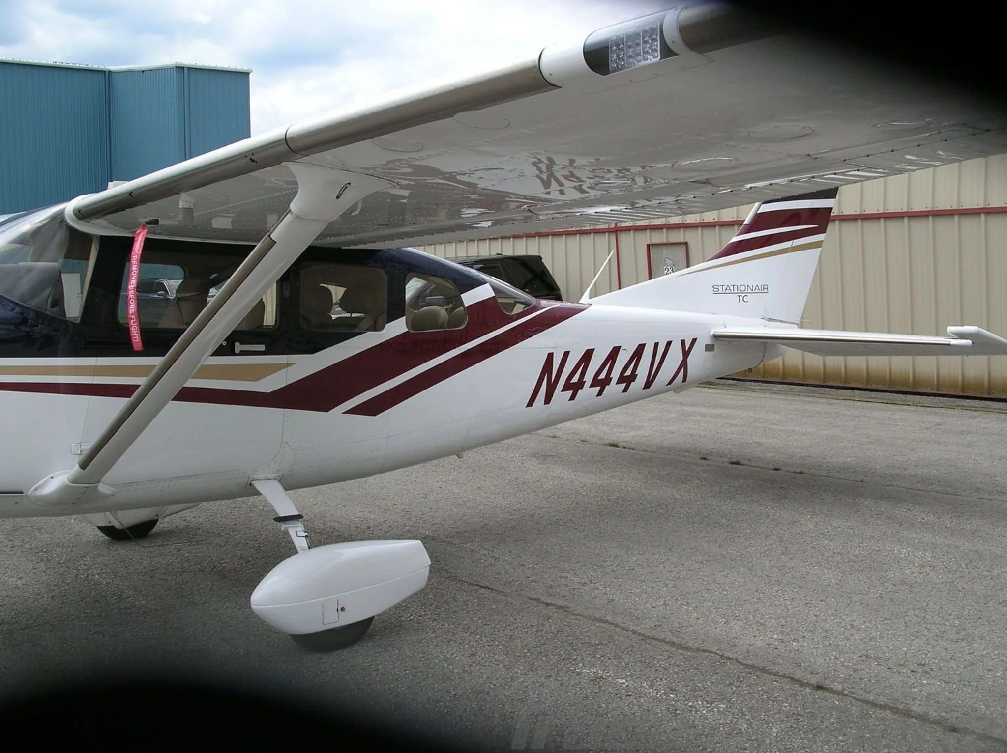 A close-up side view of the tail section of a white Cessna Stationair TC with dark blue and maroon stripes, registration N444VX, on an asphalt ramp.