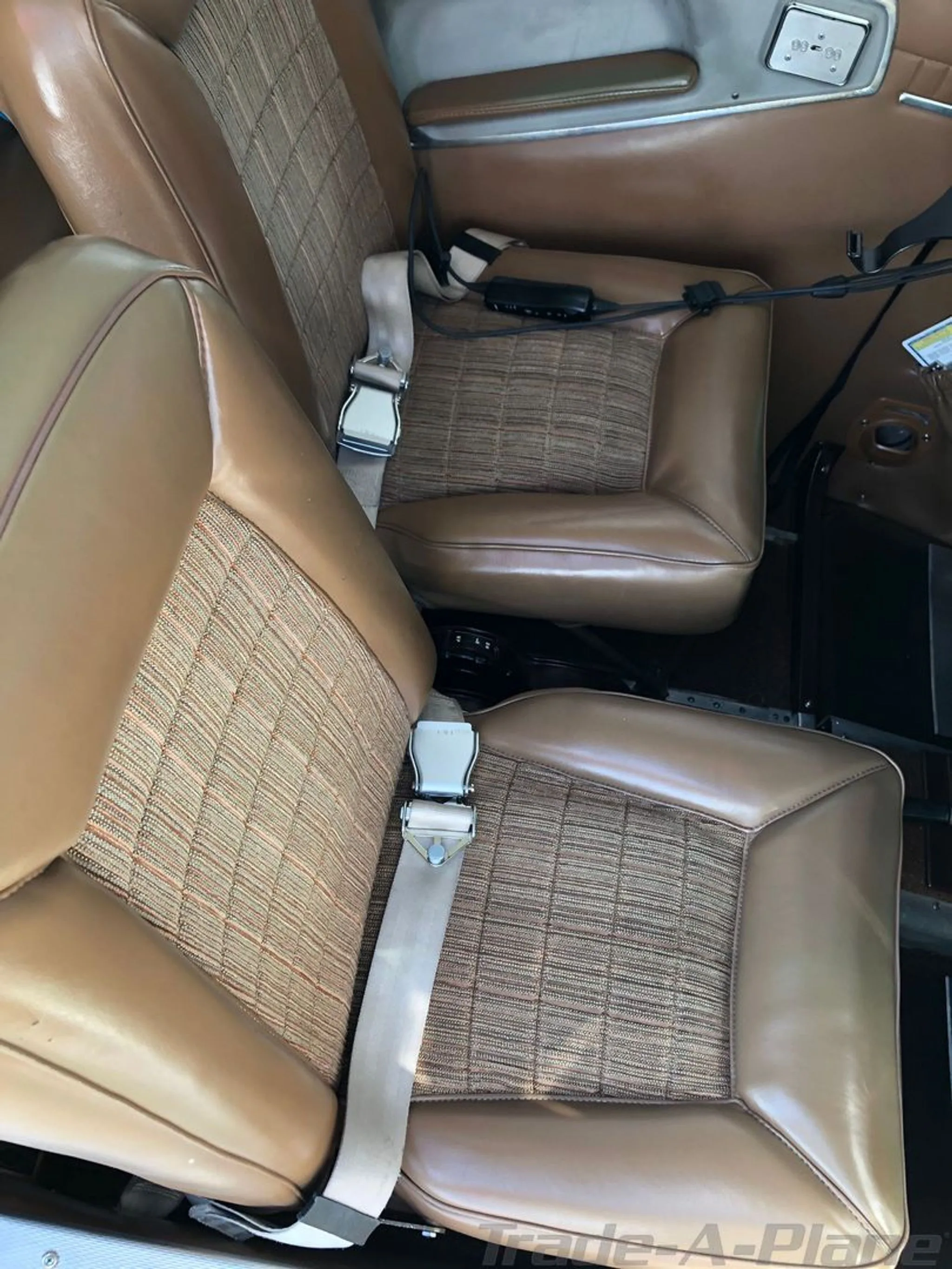 Brown and patterned fabric aircraft seats with seatbelts in the cabin interior.