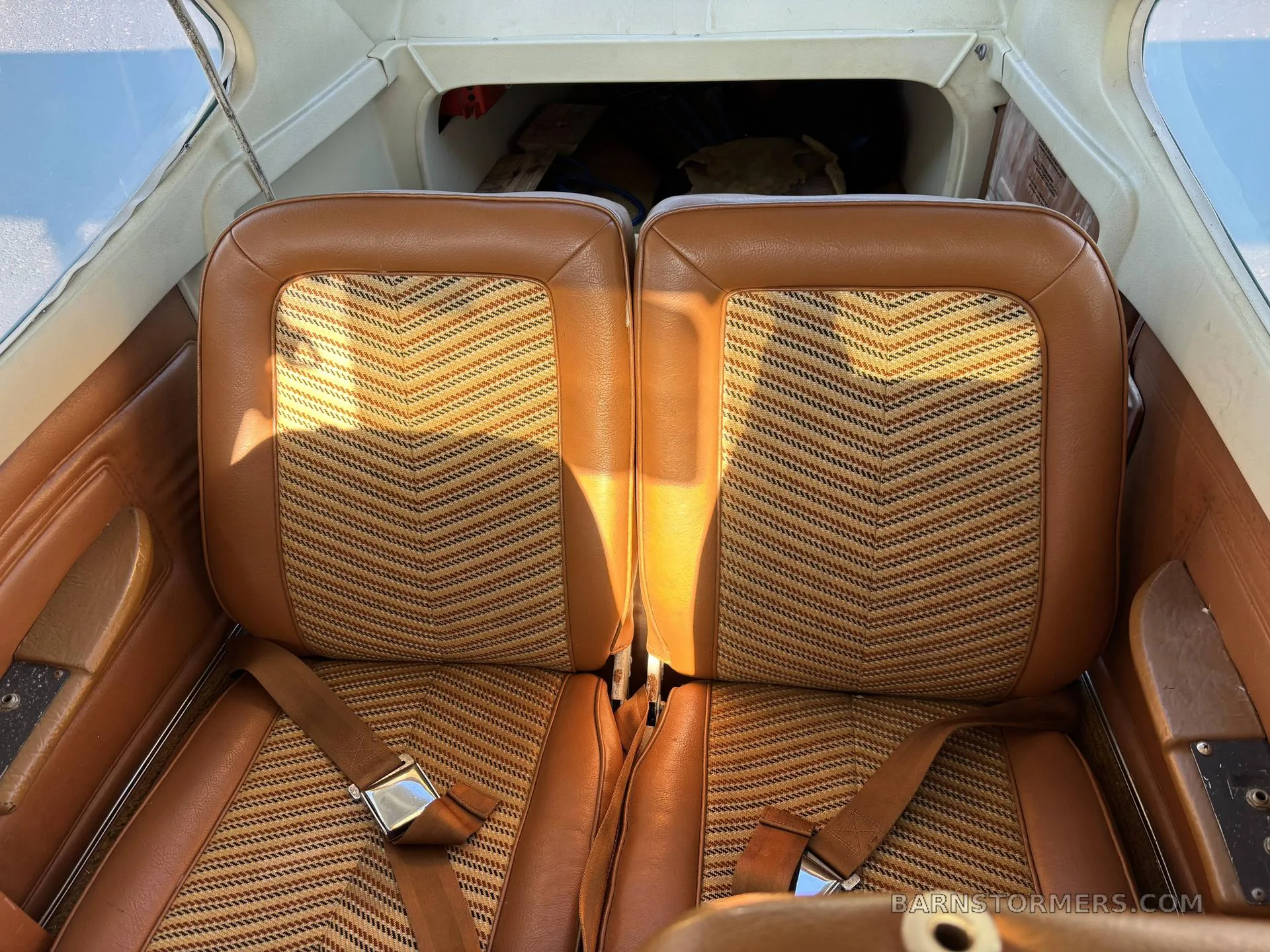 The two rear brown leather seats with patterned fabric inserts in the cabin of a small aircraft.