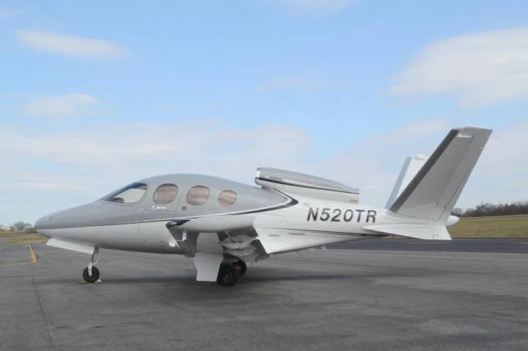 A grey and white Cirrus Vision Jet (SF50) with registration N520TR parked on an airport tarmac under a partly cloudy sky.