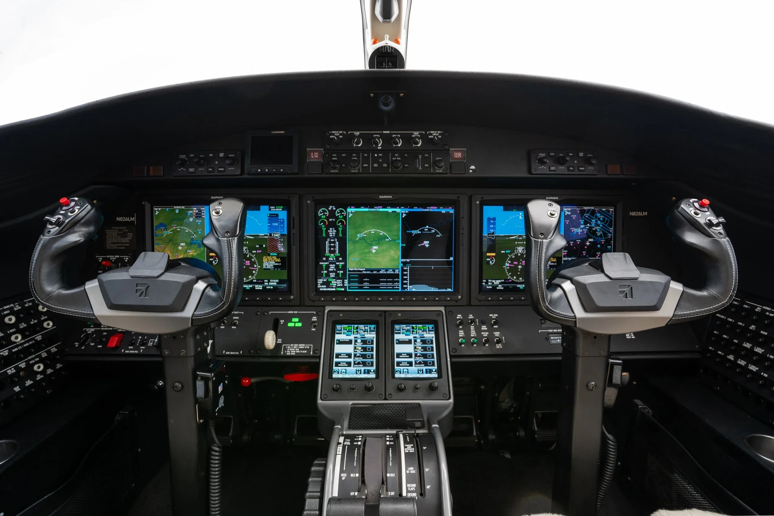 A wide view of a modern aircraft cockpit with multiple large digital displays and control yokes.