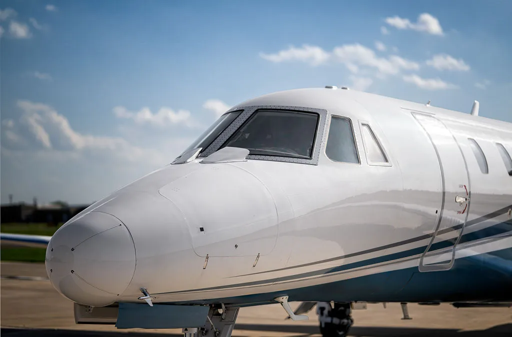 A close-up view of the nose and cockpit windows of the white and blue Cessna Citation Latitude business jet.