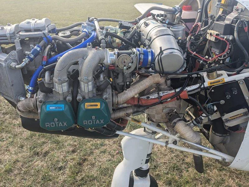 A close-up view of the Rotax engine in a light aircraft with various hoses and components visible.