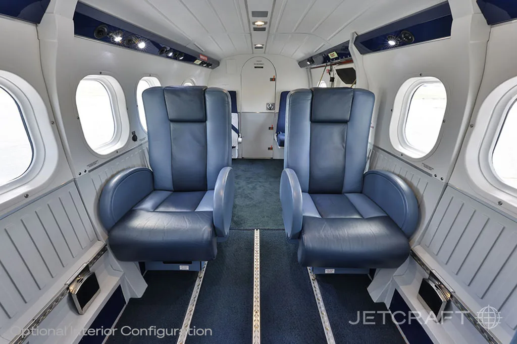 A view down the aircraft cabin aisle showing rows of blue leather seats and white interior panels.