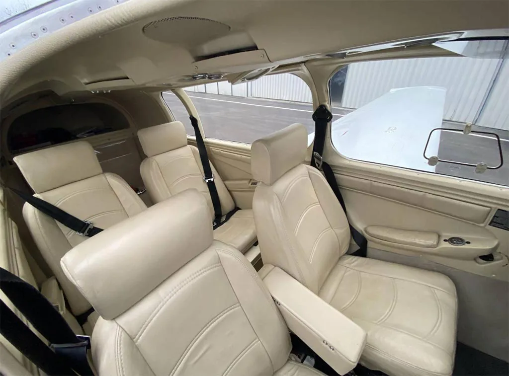 The beige leather interior of an aircraft cabin, showing four seats with seatbelts.