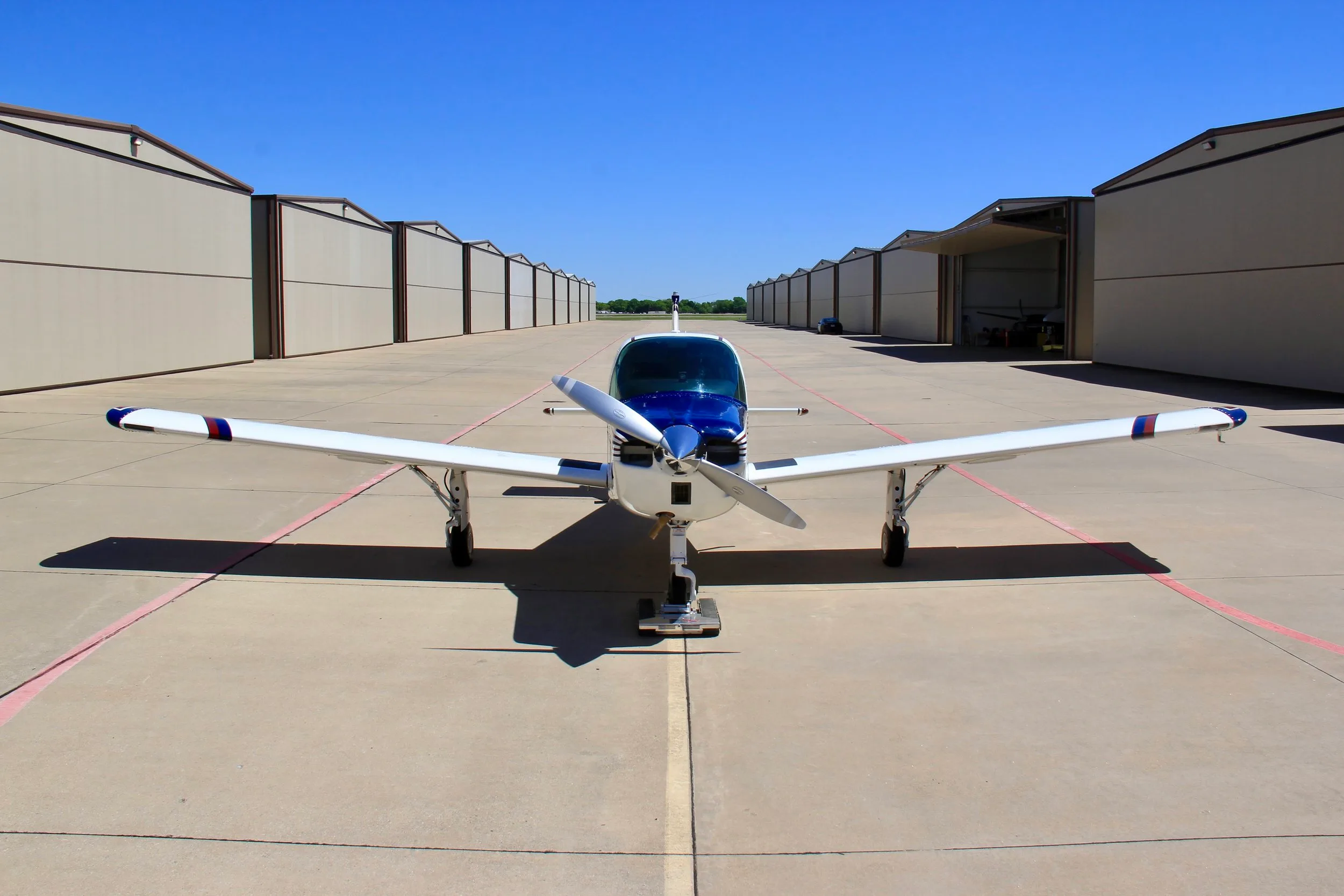 A front view of the white, blue, and red single-engine aircraft (N66304) on an airport tarmac between hangars.