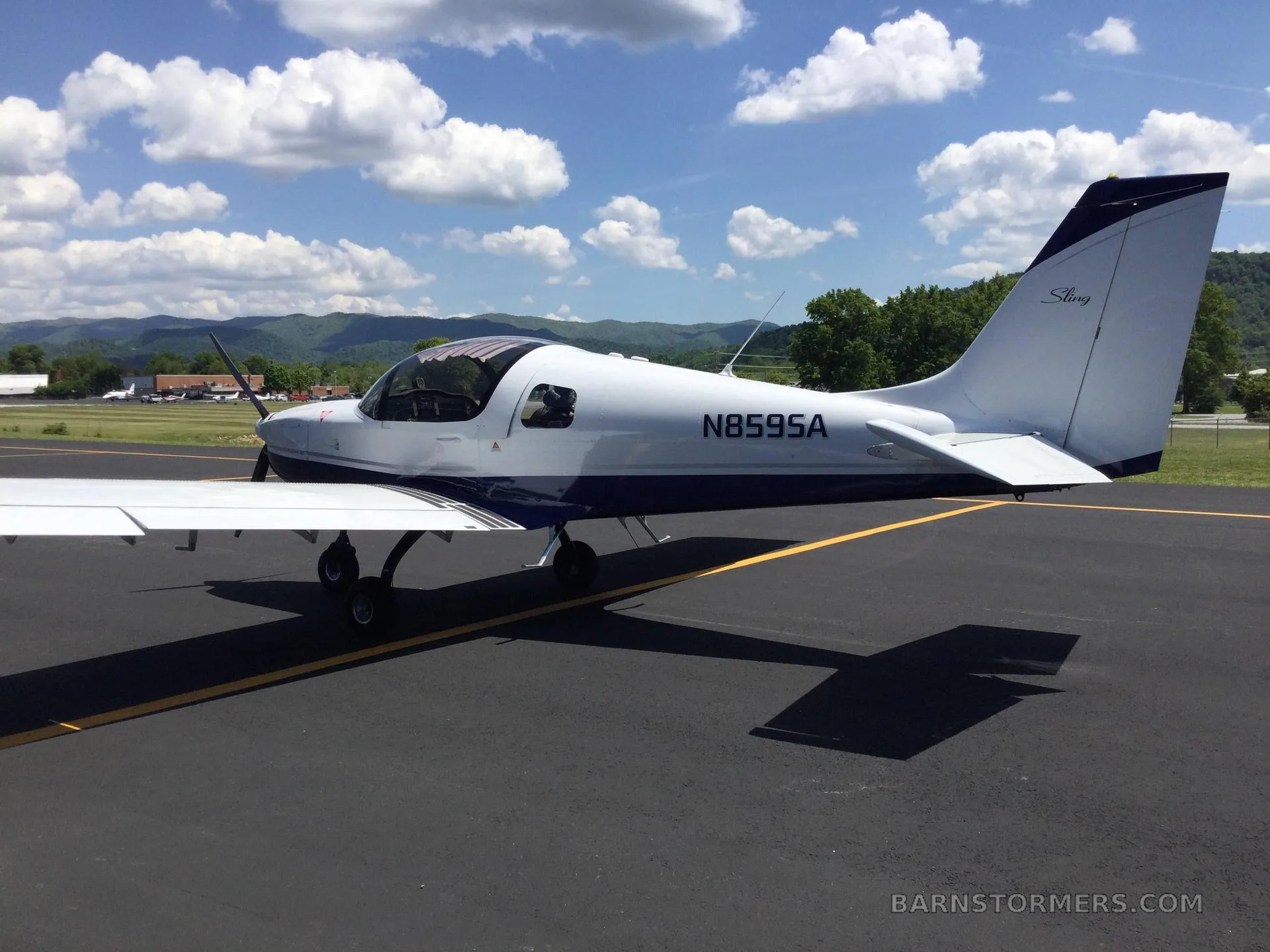 A white and blue Sling aircraft with registration N859SA is parked on an asphalt runway, viewed from the rear-right.