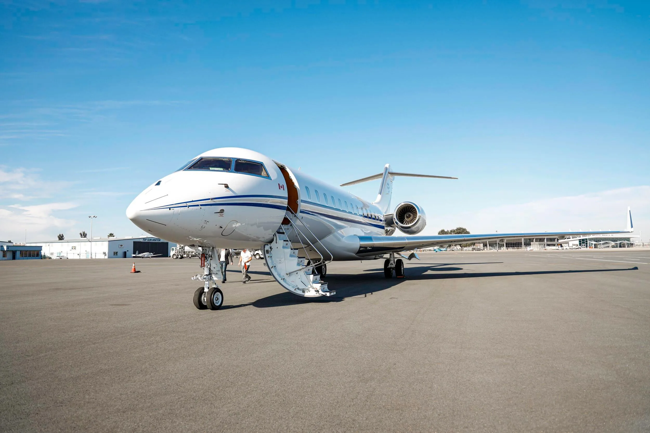 A white private jet with blue stripes is parked on an airport tarmac with its main door open and stairs extended.