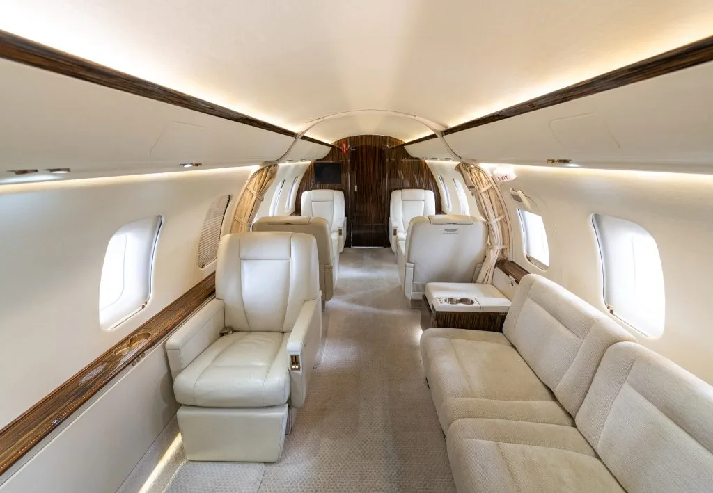 The luxurious interior cabin of a business jet with cream leather seats and dark wood paneling.