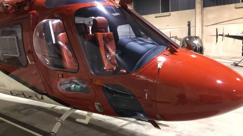 A close-up view of the nose and cockpit area of a red and white helicopter in a hangar.