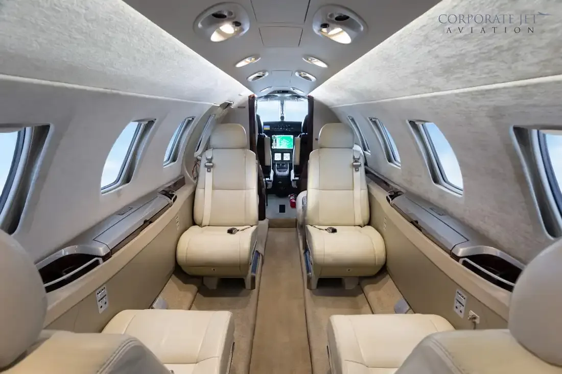 The interior of a private jet cabin with light-colored leather seats and a view into the cockpit.