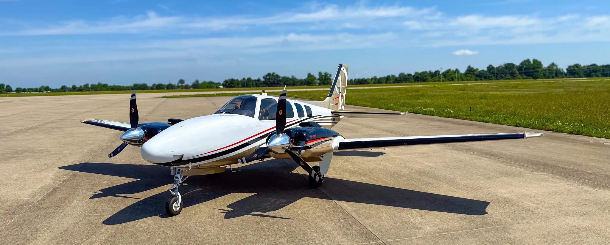 Three-quarter front view of a white and gold twin-engine Beechcraft Baron G58 on an airfield.