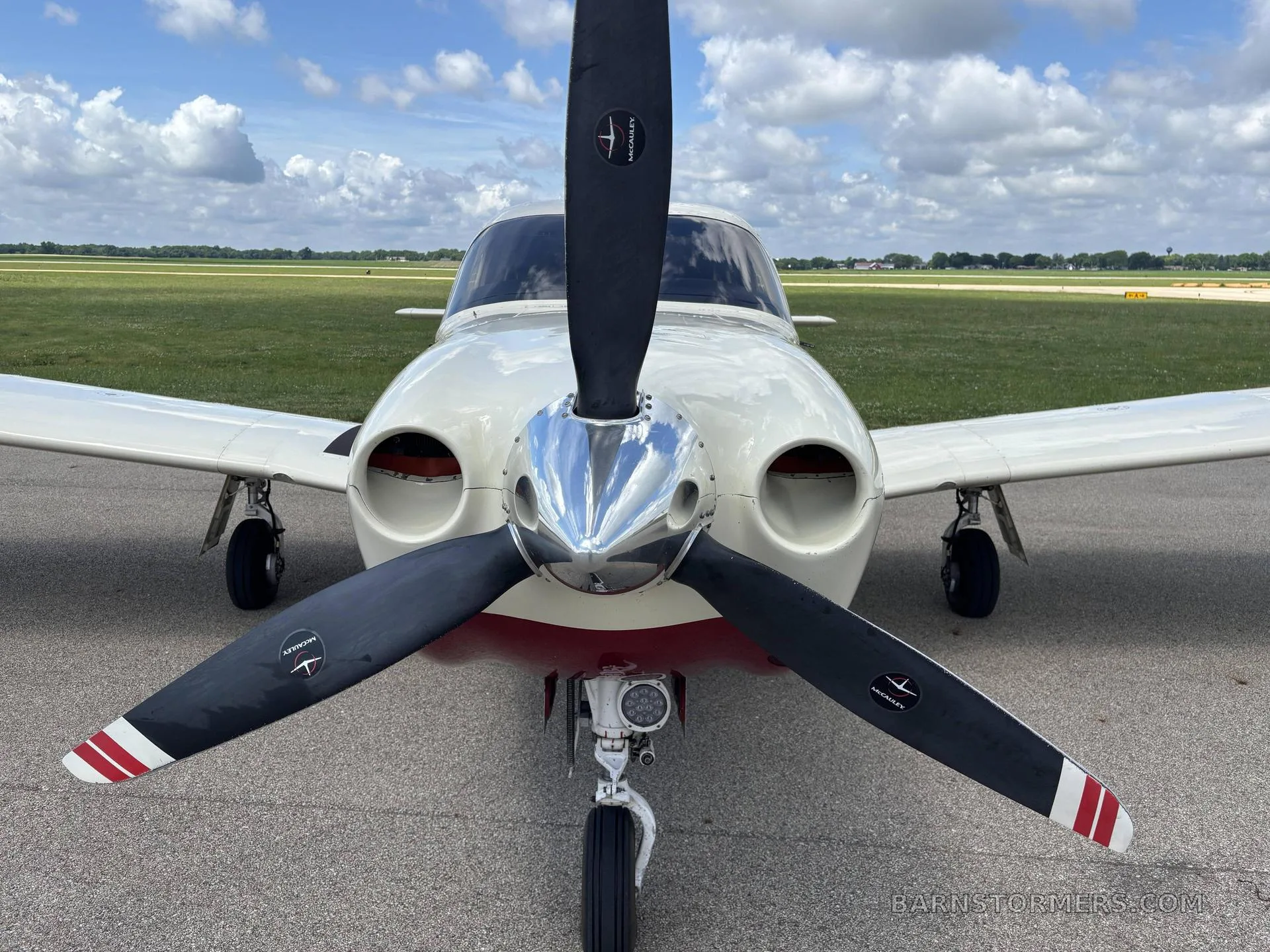 A close-up front view of the white and red Piper Saratoga II HP aircraft, showing its propeller and nose.