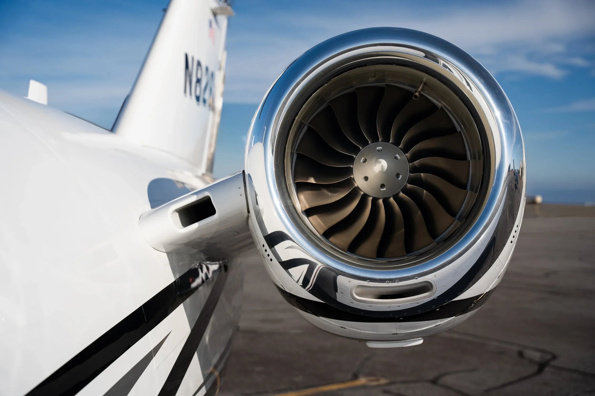 Close-up of a shiny chrome jet engine on the tail of a white aircraft with registration N826LM.