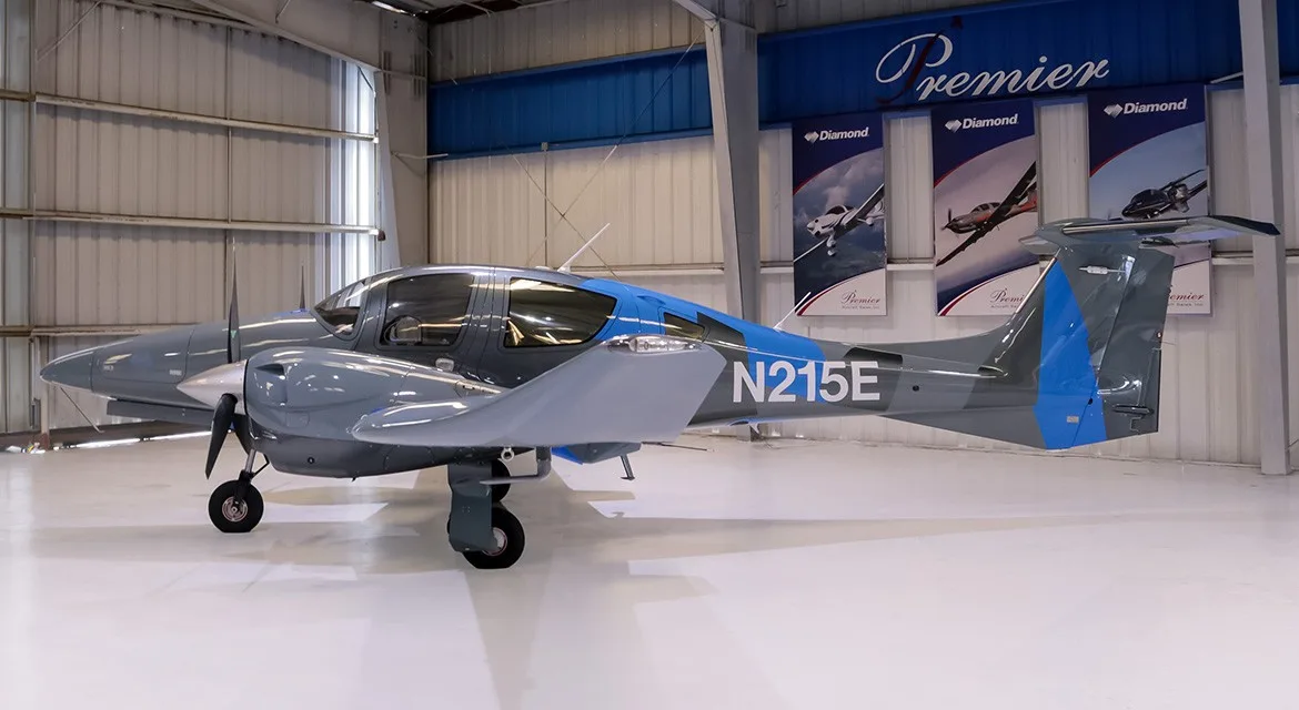 A side view of a gray and blue Diamond DA62 aircraft, registration N215E, parked inside a hangar.