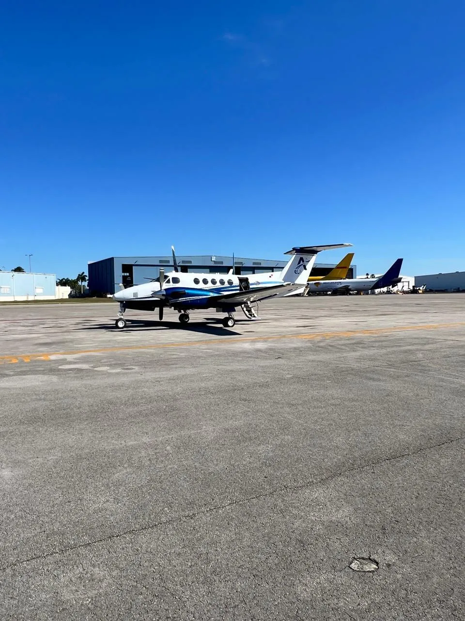 A white and blue turboprop aircraft (King Air) with registration HP-5DMB parked on an airport tarmac under a clear blue sky.