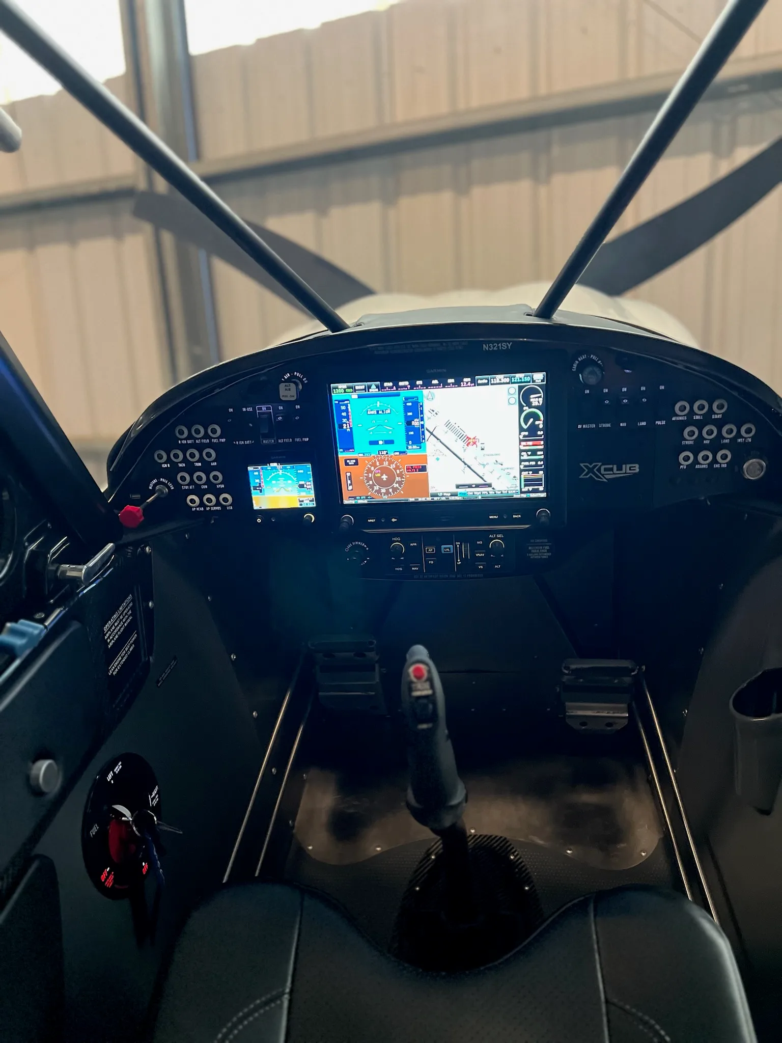 The cockpit of an X-Cub aircraft, featuring a modern instrument panel with multiple digital displays and a central joystick.