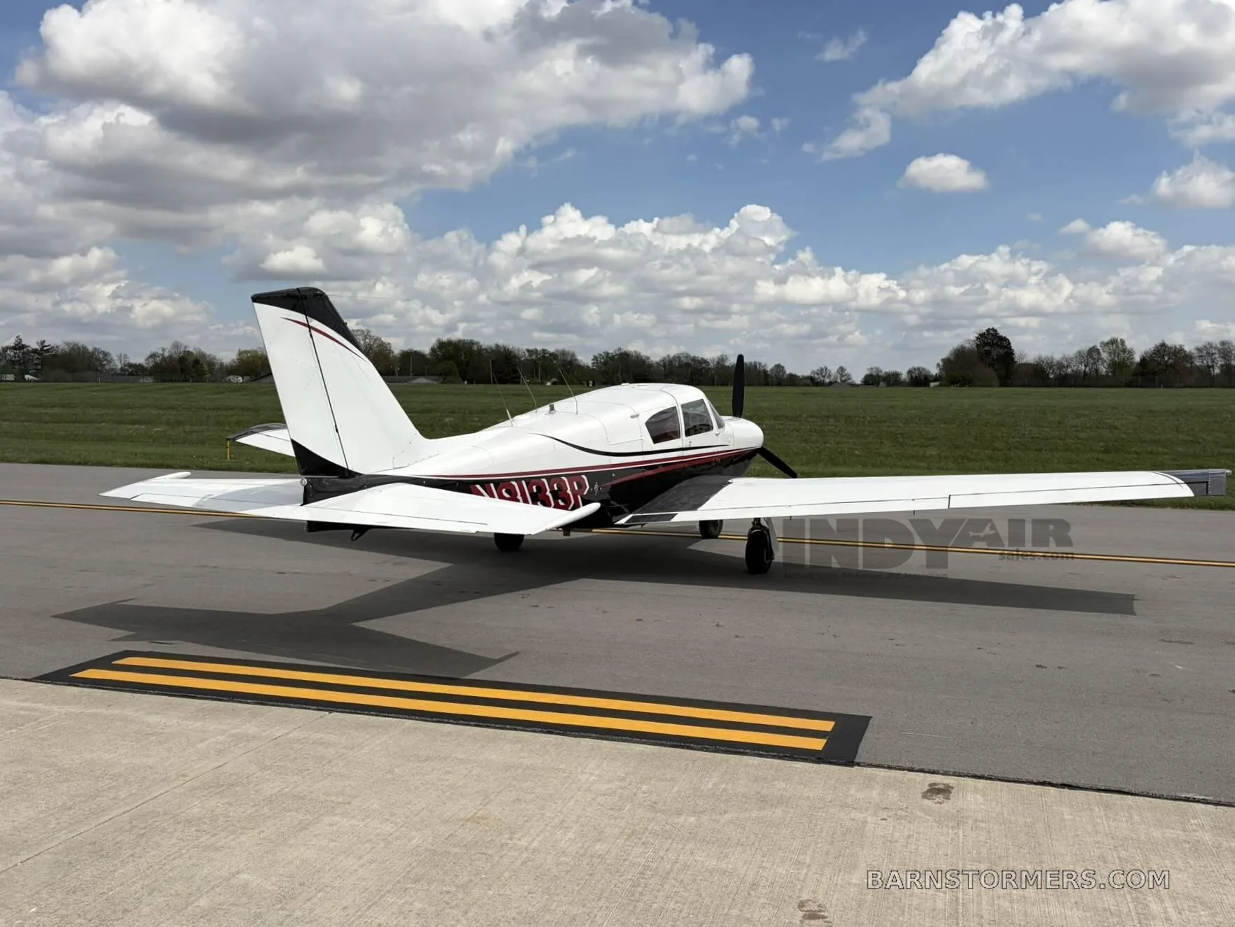 A white and black single-engine propeller aircraft with red accents, viewed from the rear-right, parked on an asphalt taxiway.