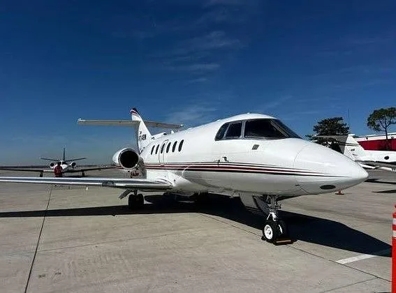 A white Hawker business jet with red and black stripes, tail number N714BW, parked on an airfield under a clear blue sky.