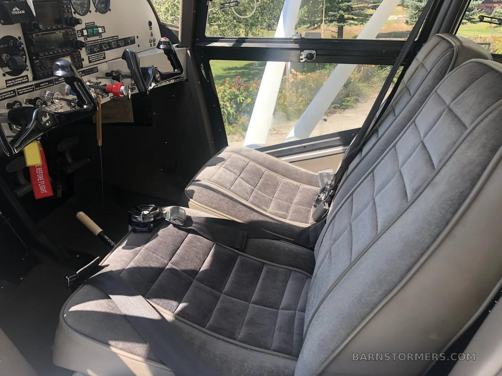 The interior cabin of a floatplane, showing two grey quilted seats and part of the cockpit.