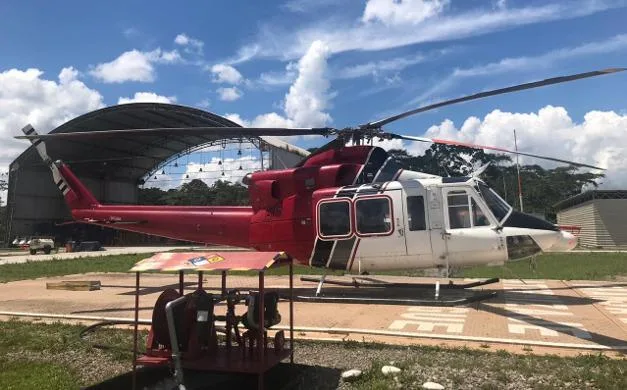 A red, white, and black Bell 412 helicopter parked on a helipad with a hangar in the background.