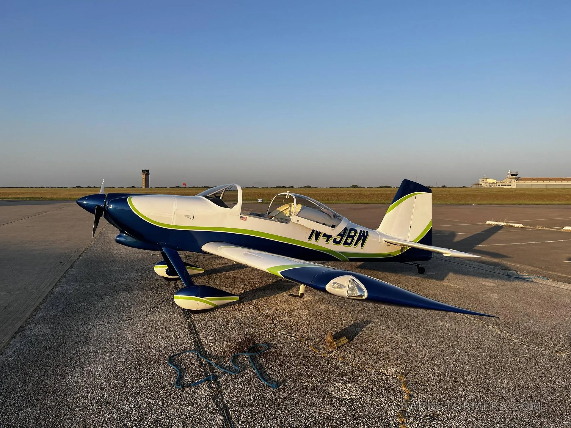 A blue and white experimental aircraft with green stripes, registration N49BW, parked on an airfield with a control tower in the background.