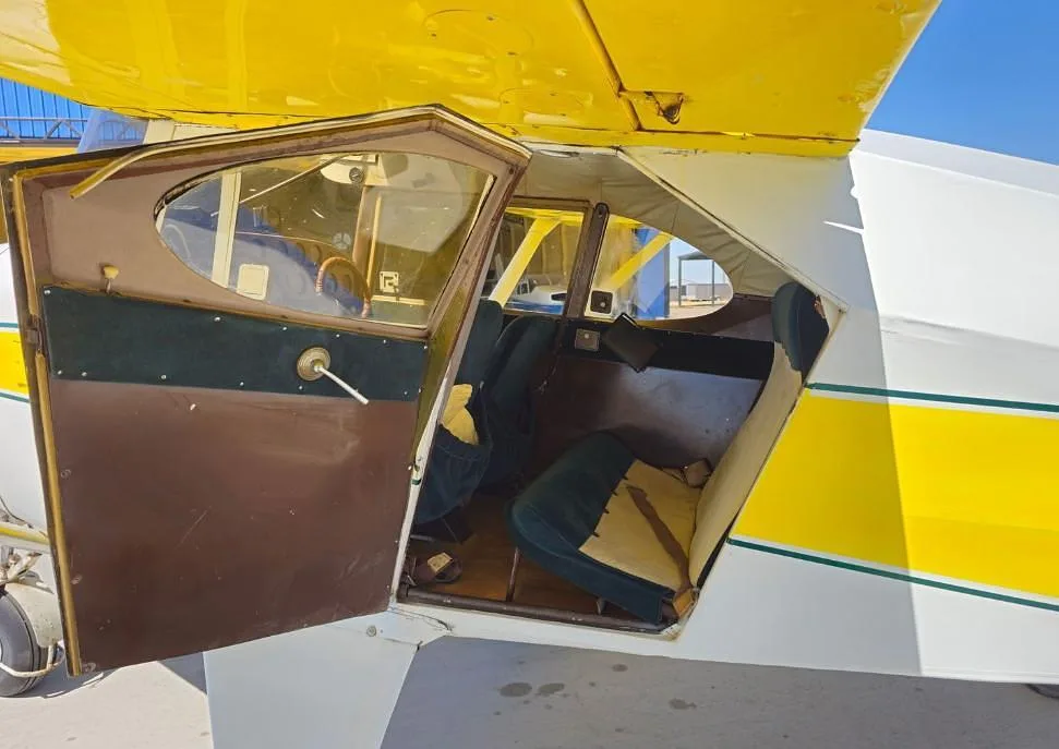 The open door of a white and yellow Piper PA-12 Super Cruiser revealing the two-seat cabin interior.