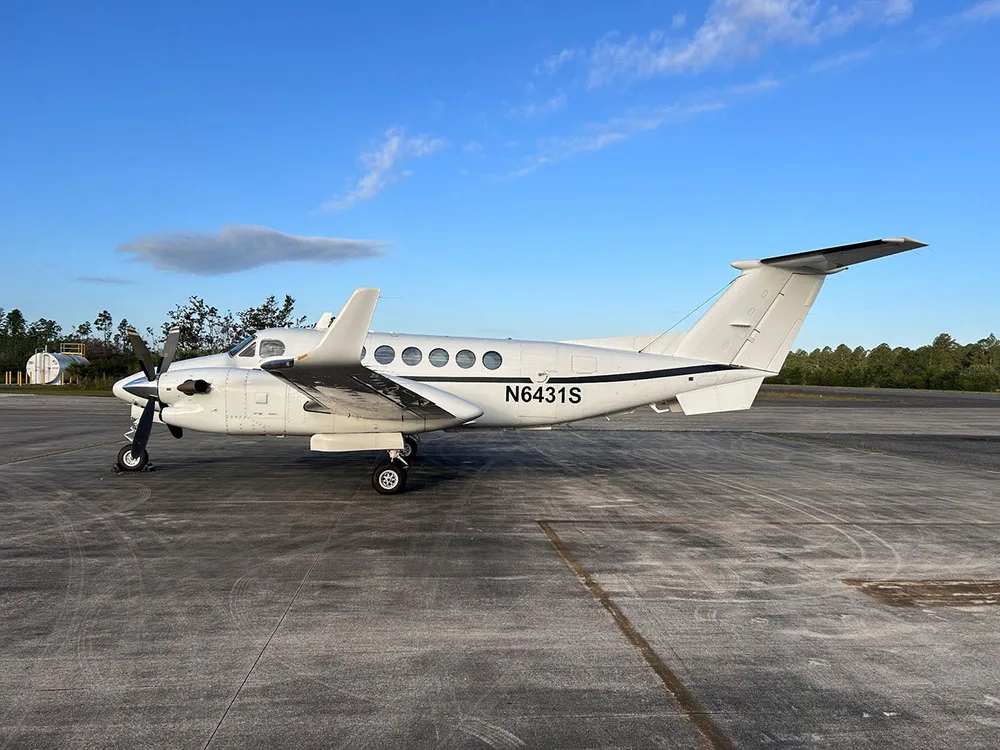 A white Beechcraft King Air 350 turboprop aircraft with registration N6431S is parked on an asphalt tarmac under a blue sky.