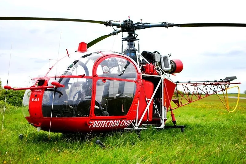 A red "PROTECTION CIVILE" helicopter with a bubble canopy sits in a grassy field.