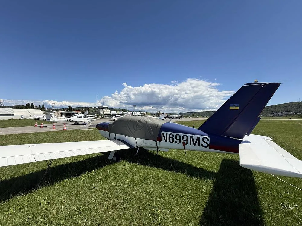 A blue and white Socata Trinidad aircraft, N699MS, is parked on a grassy area with a cockpit cover.